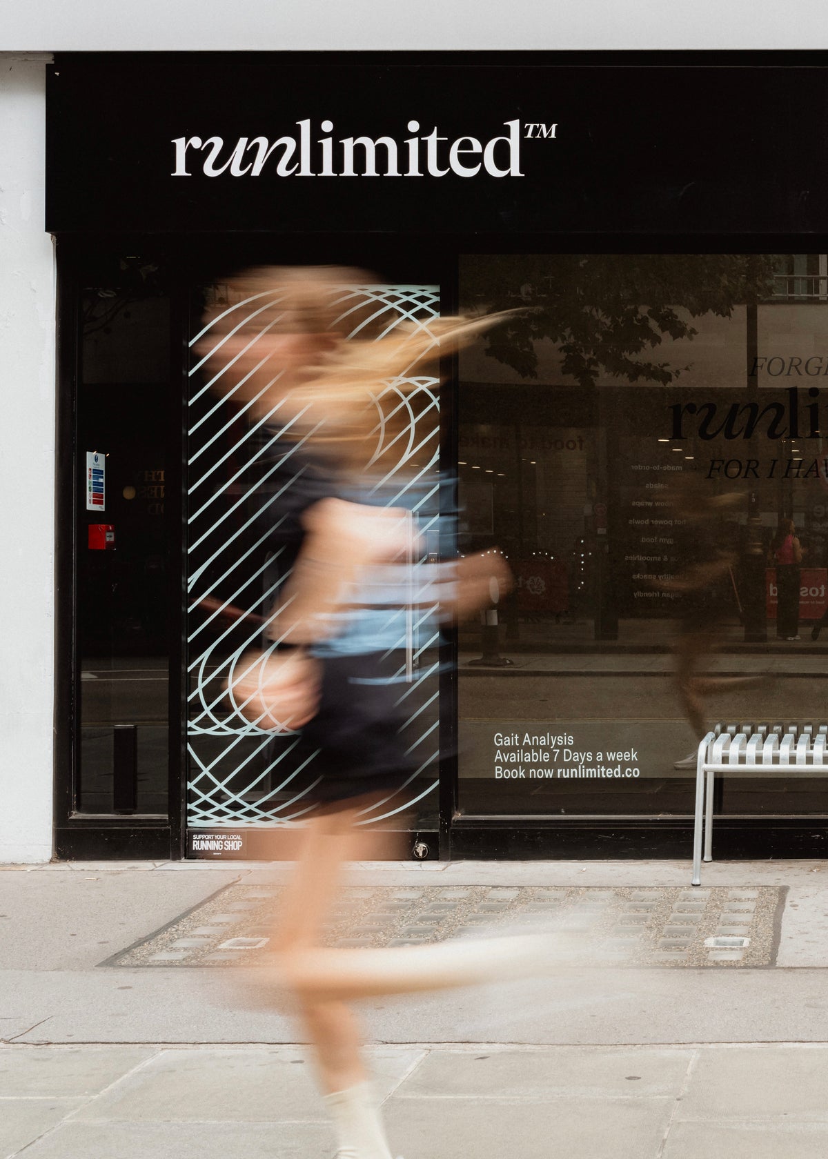 Person walking past a store with 'runlimited' branding on a city street.